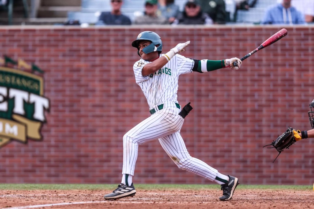 Alejandro Garza, wearing a white baseball uniform, follows through on a swing.
