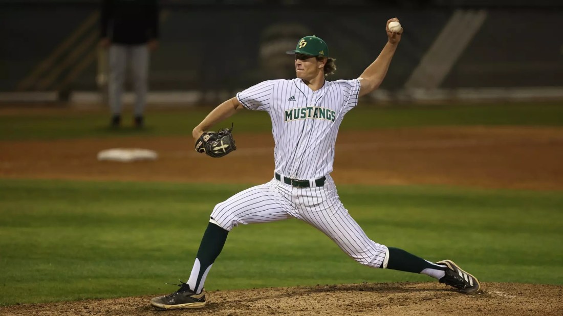 Chris Downs delivers a pitch in a white Cal Poly uniform.